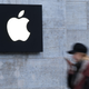 A woman, blurred, walks in front of an Apple store logo